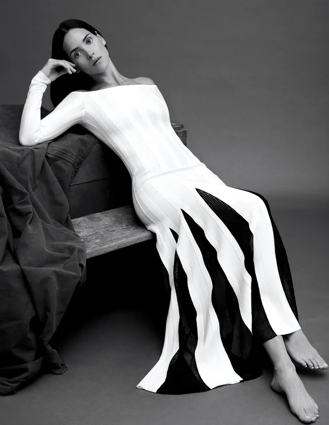 Adria Arjona sitting barefoot in a white dress for a monochrome portrait.