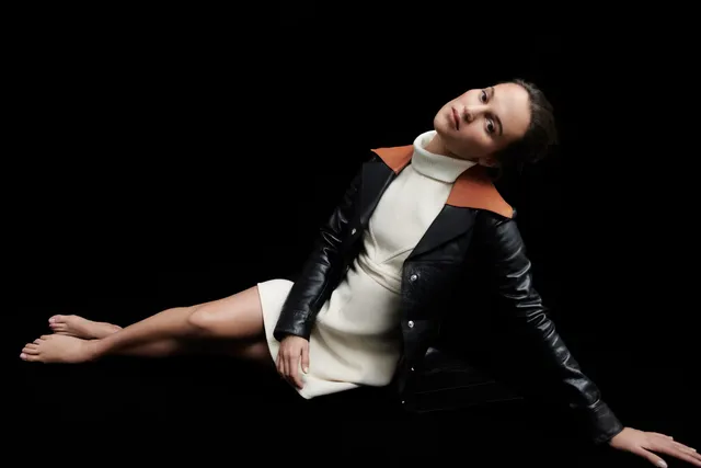 Alicia Vikander reclining in a dark studio fashion portrait.
