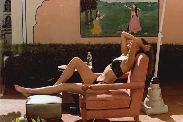 Josephine Skriver reclining barefoot in an outdoor chair beside a floor lamp.