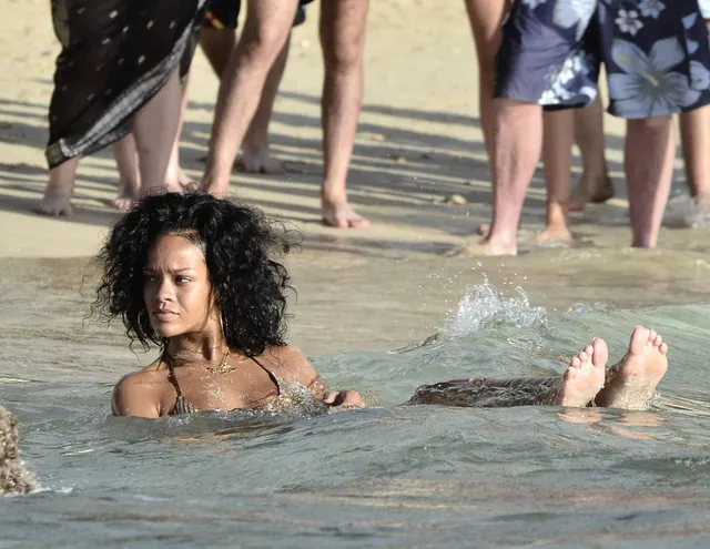 Rihanna floating in shallow water with bare soles raised.