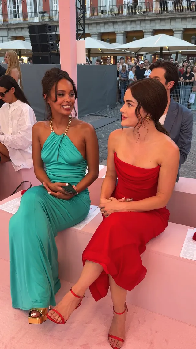 Lucy Hale sitting with a companion in a red dress at an event.