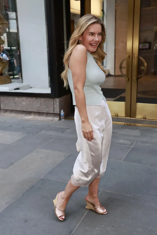 Elisha Cuthbert walking outdoors in a satin skirt and wedge heels.