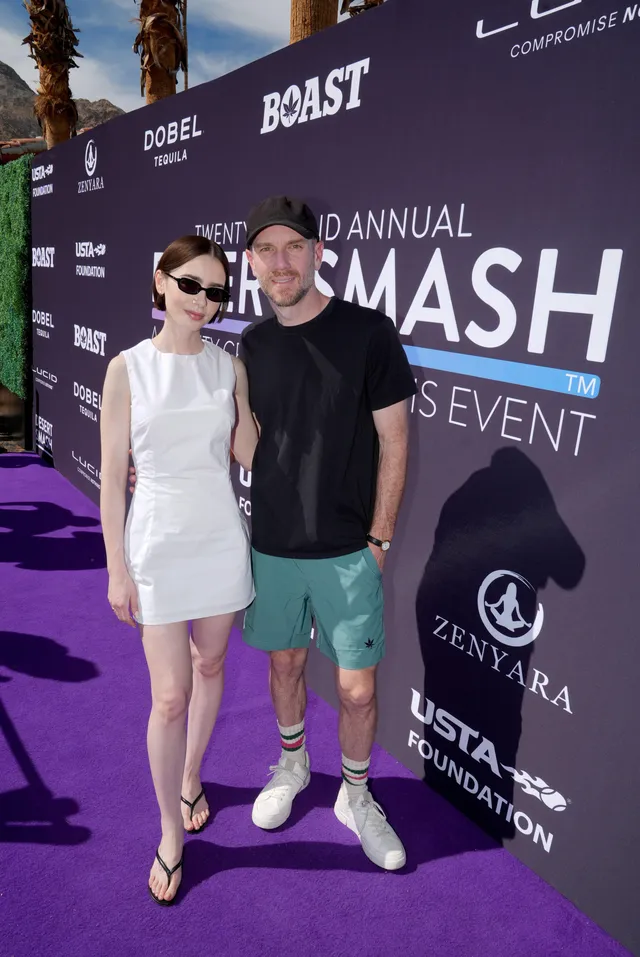 Lily Collins posing beside a man in a white outfit and flat sandals.