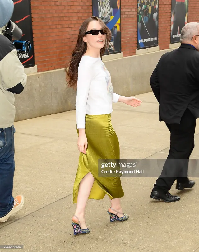 Victoria Pedretti walking outdoors in a white top and green skirt.