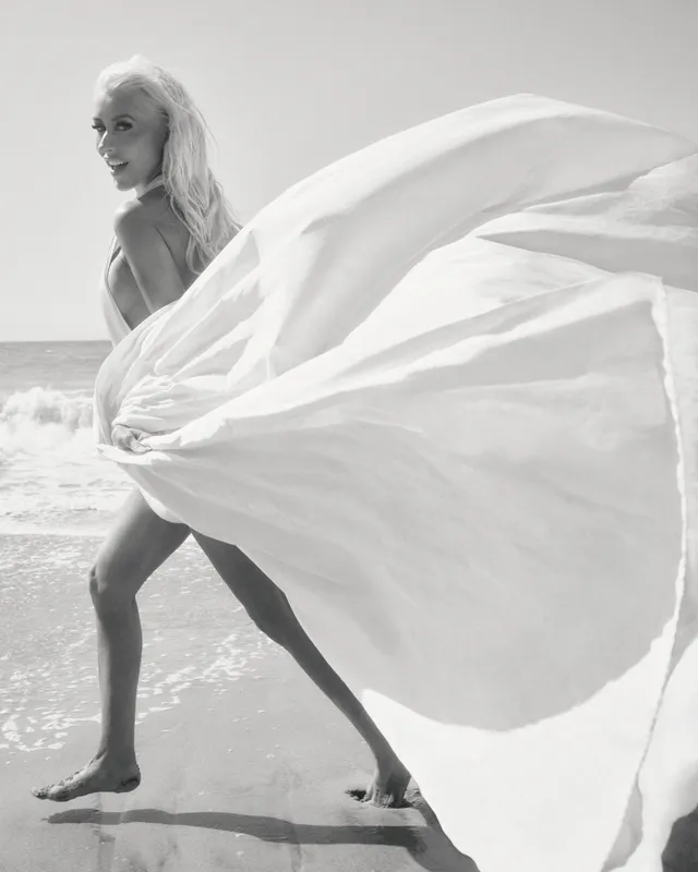 Christina Aguilera walking barefoot beside the sea with flowing white fabric.