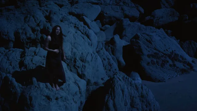 Mackenzie Ziegler standing by coastal rocks in a dark scene.