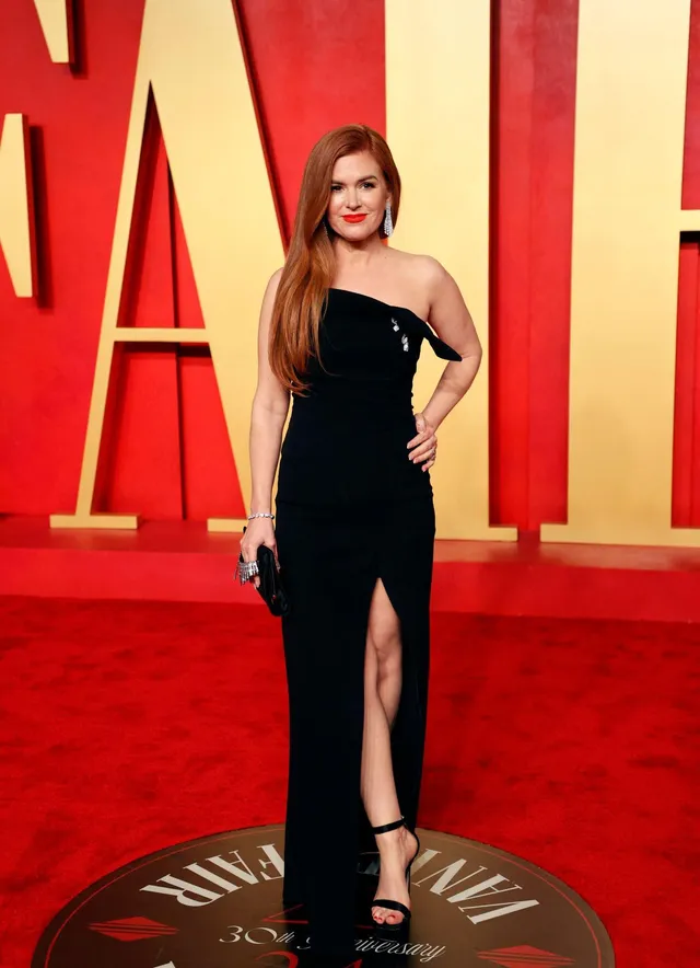 Isla Fisher posing at an event in a long black outfit.