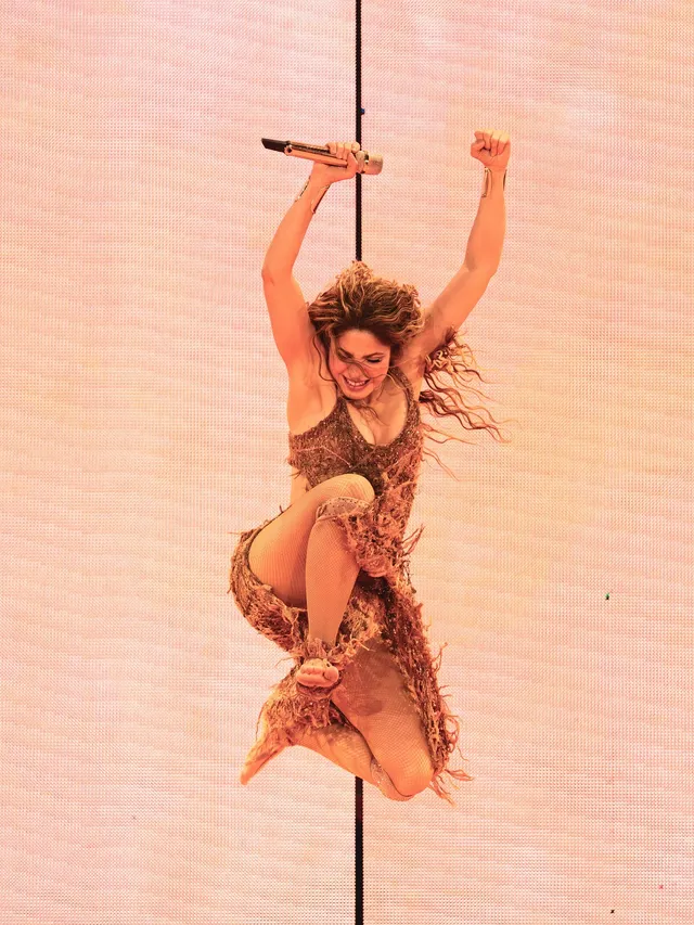 Shakira singing barefoot while holding a stage pole.