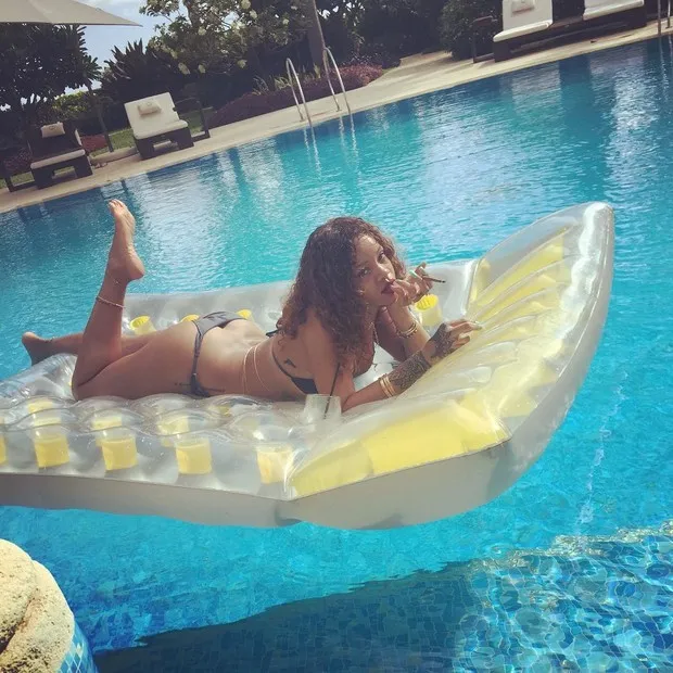 Rihanna reclining barefoot on a yellow pool float.