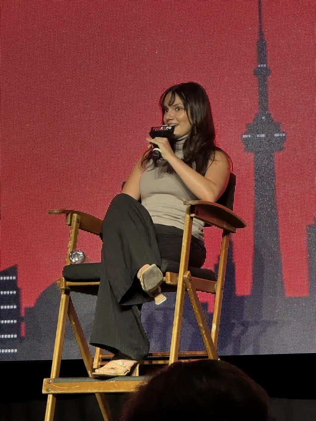 Dafne Keen sitting onstage in dark socks and casual shoes.