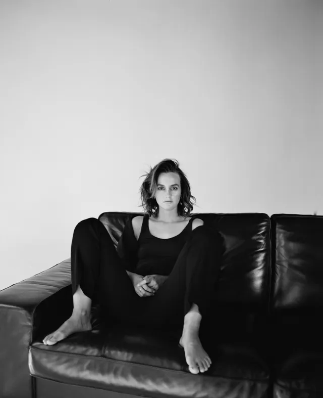 Leighton Meester sitting on a leather sofa in a dark outfit.