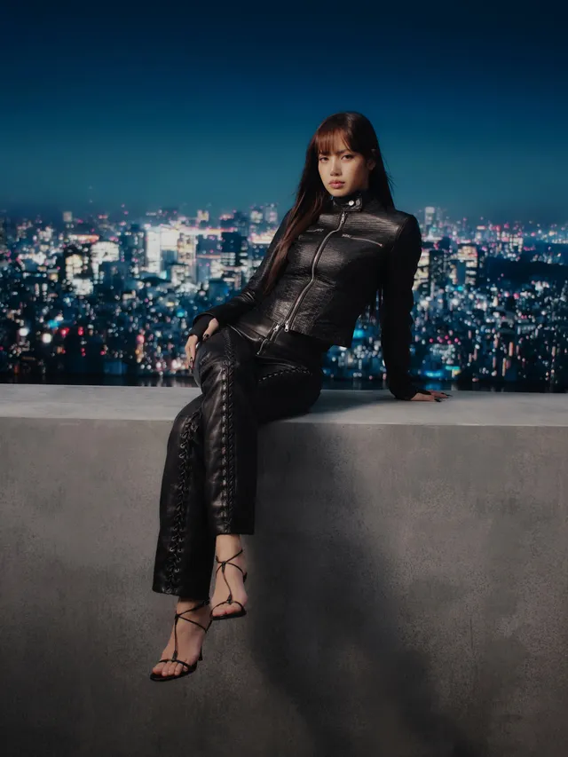 Lisa (Lalisa Manobal) sitting in dark heeled sandals and a dark outfit against a city backdrop.