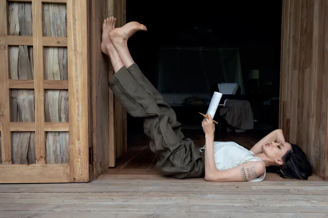 Angelina Jolie lying on a wooden floor while reading a book.