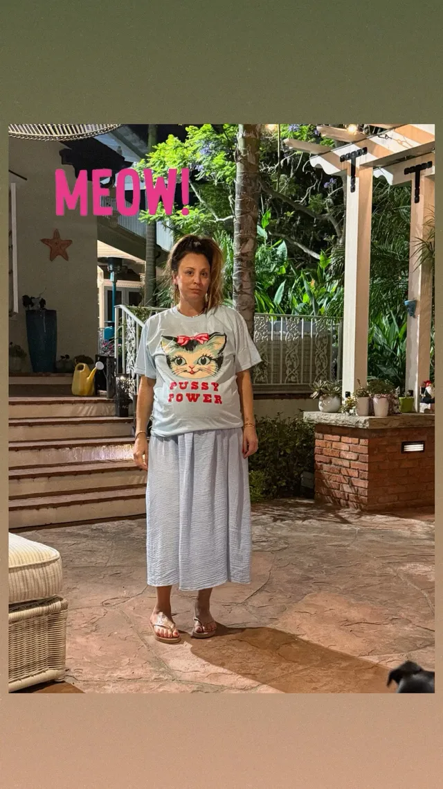 Kaley Cuoco standing on a patio in a long skirt and flip-flops.