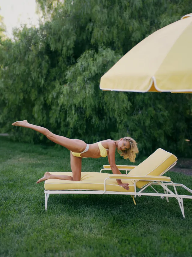 Elsa Hosk stretching barefoot on a garden lounger beside a parasol.