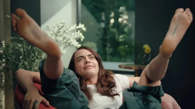 Cara Delevingne reclining outdoors with her feet raised.