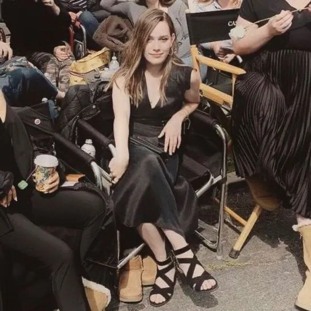 Victoria Pedretti sitting in a backstage chair in a black outfit.