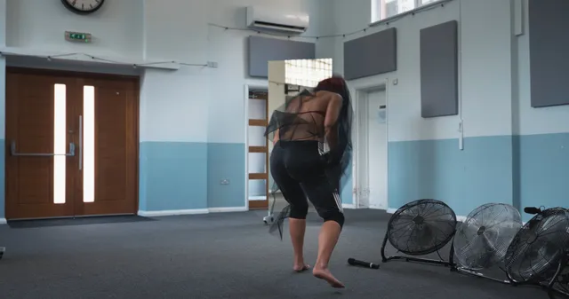 Naomi Scott standing barefoot beside fans in a rehearsal room.