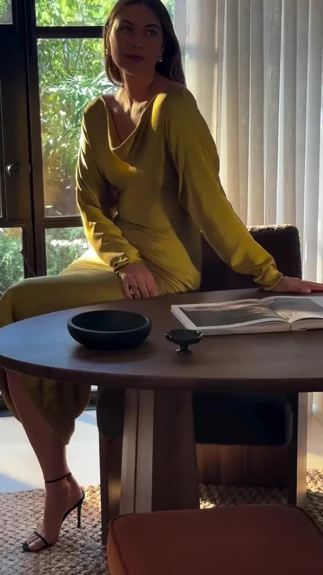 Maria Sharapova sitting in heeled sandals and a green dress beside a table.