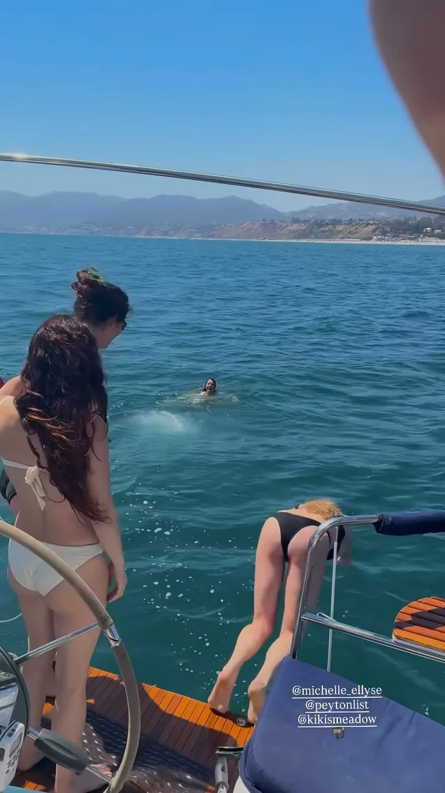 Peyton List standing on a boat beside swimmers.