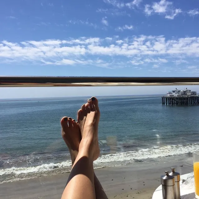 Gemma Chan resting with her feet raised toward a view of the sea.