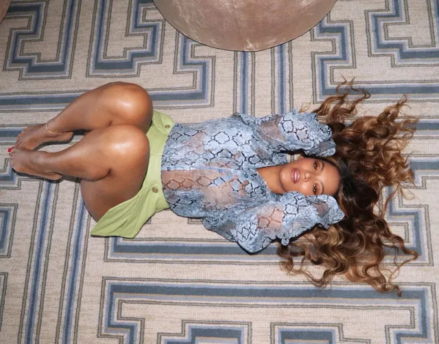 Beyoncé lying on a patterned floor in a casual outfit.