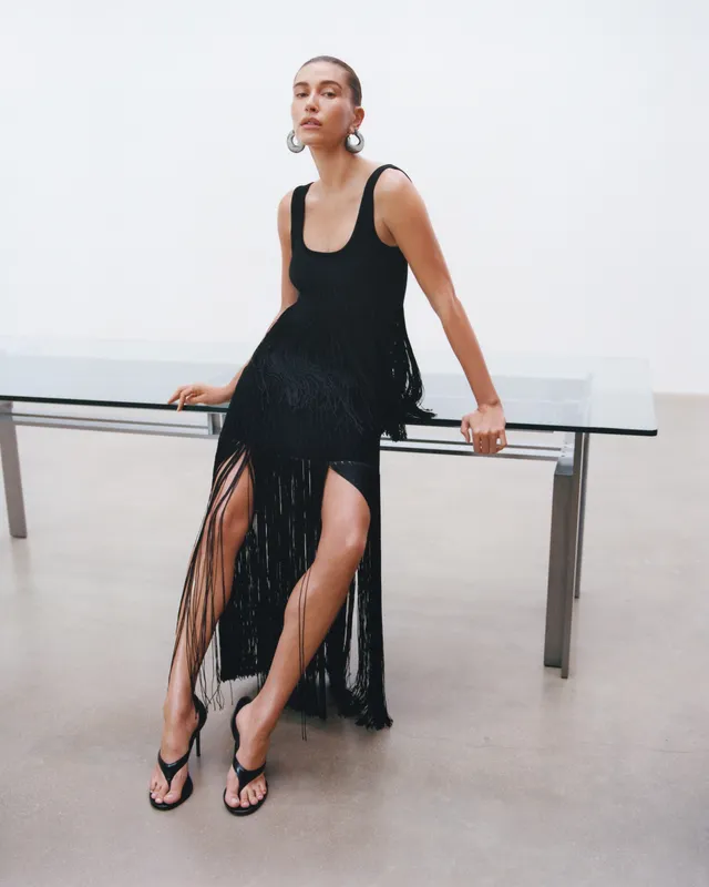 Hailey Bieber wearing a black dress and casual sandals in a studio.