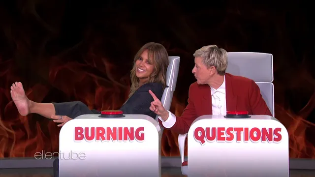 Halle Berry sitting barefoot on a television set beside the host.