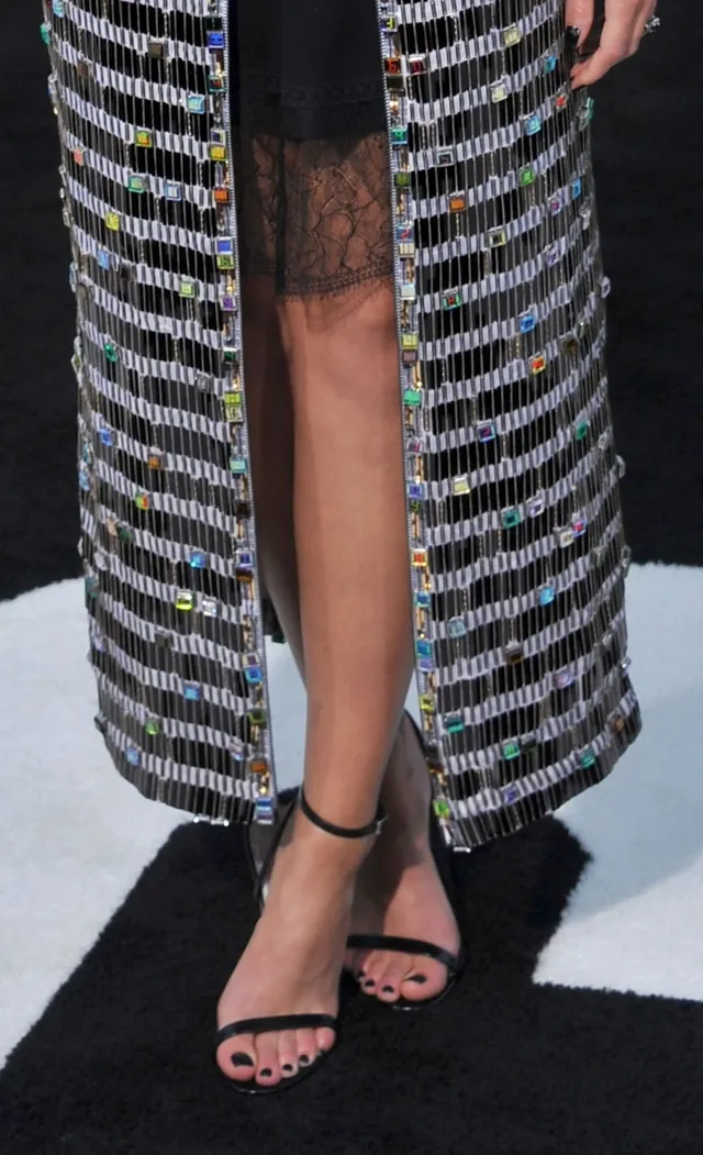 Naomi Scott wearing black heels beneath a patterned skirt.