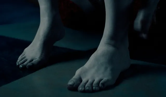 Monica Bellucci standing barefoot in a dimly lit screen scene.