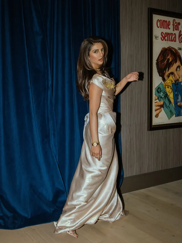Priyanka Chopra Jonas wearing heeled sandals beneath a long silver dress at an indoor event.