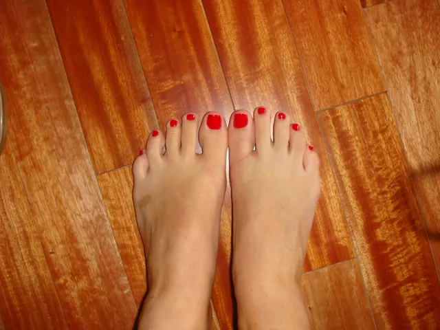 Olivia Munn showing red-painted toenails above a wooden floor.
