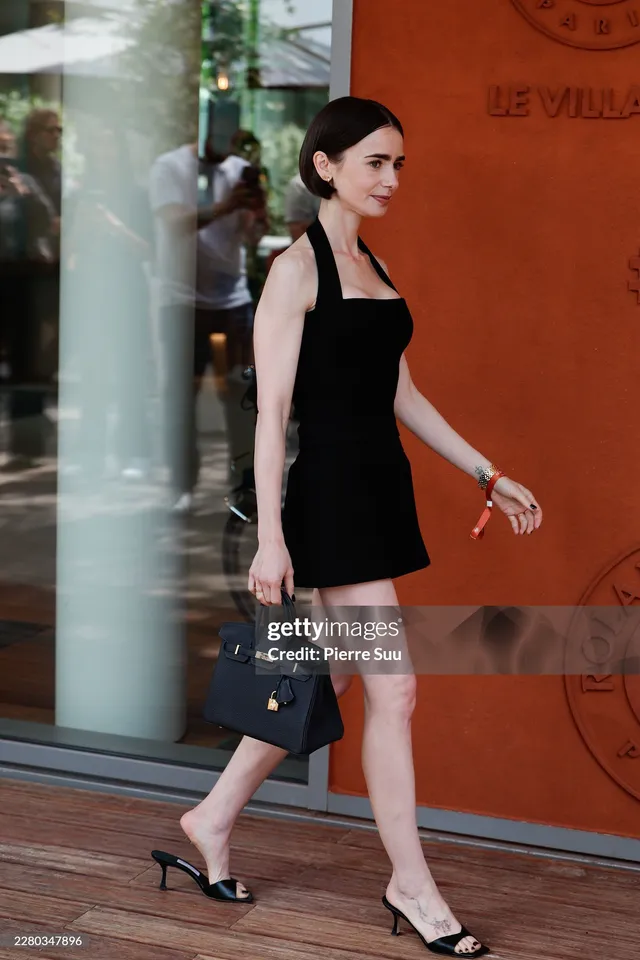 Lily Collins walking outside in a black dress and black heels.