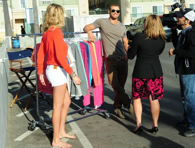 Kate Upton standing barefoot beside other people at a clothes rack.