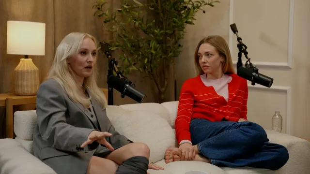 Amanda Seyfried sitting cross-legged barefoot beside another guest on a couch.