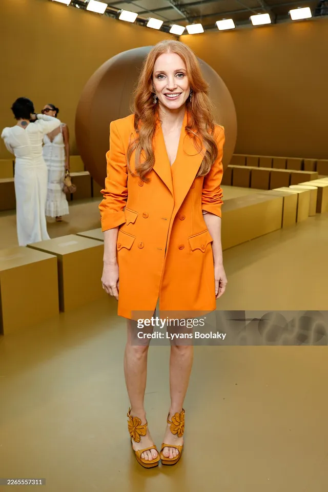 Jessica Chastain standing in an orange jacket at a fashion event.