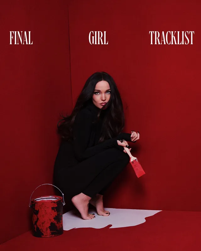 Dove Cameron crouching barefoot for a red studio portrait.