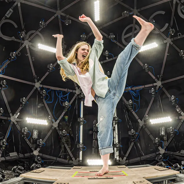 Elle Fanning balancing barefoot on a platform in jeans and a light jacket.