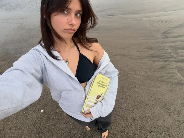 Nicole Wallace taking a beach selfie in a pale shirt over dark swimwear.