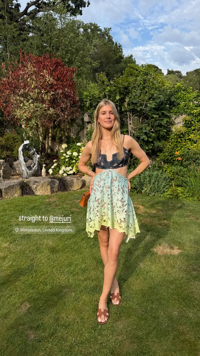 Eugenie Bouchard standing in heeled sandals and a short pale dress on a lawn.