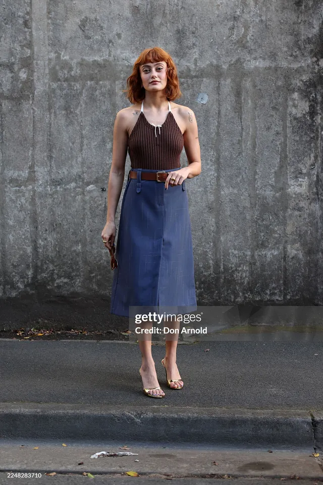 Ella Purnell posing against a textured wall in a blue skirt.