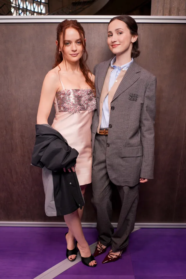 Joey King posing beside another woman in a pale dress and black heels.