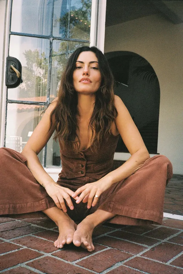 Phoebe Tonkin sitting on a tiled patio in a brown outfit.