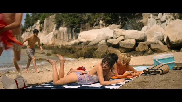 Emily Alyn Lind reclining barefoot with a group on a beach blanket.