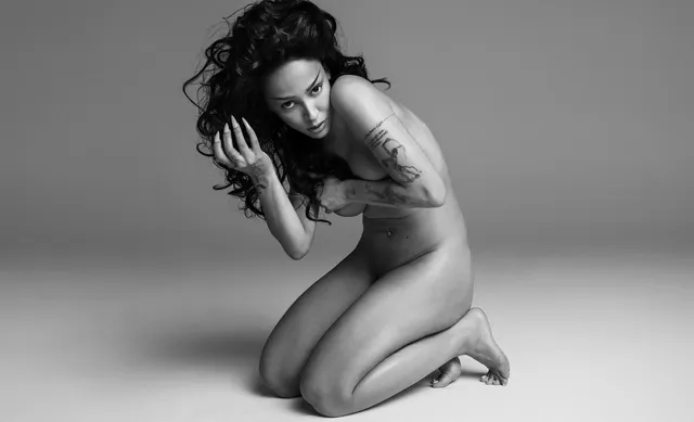 Doja Cat kneeling barefoot in a monochrome studio portrait.