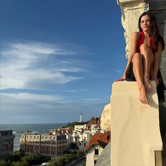 Danielle Campbell sitting on a wall overlooking a coastal town.