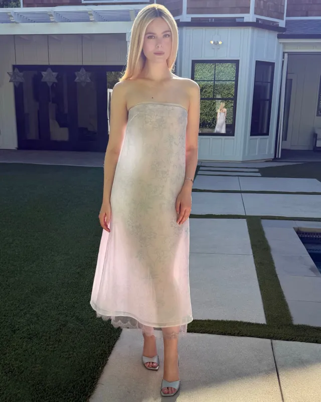 Elle Fanning wearing a pale dress and heeled sandals outdoors.