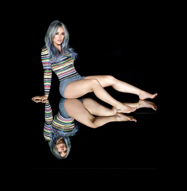 Hilary Duff sitting barefoot on a reflective studio floor.