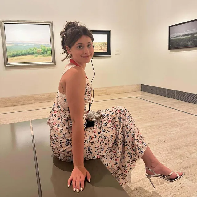 Nicole Wallace sitting indoors in a floral dress and clear heels.