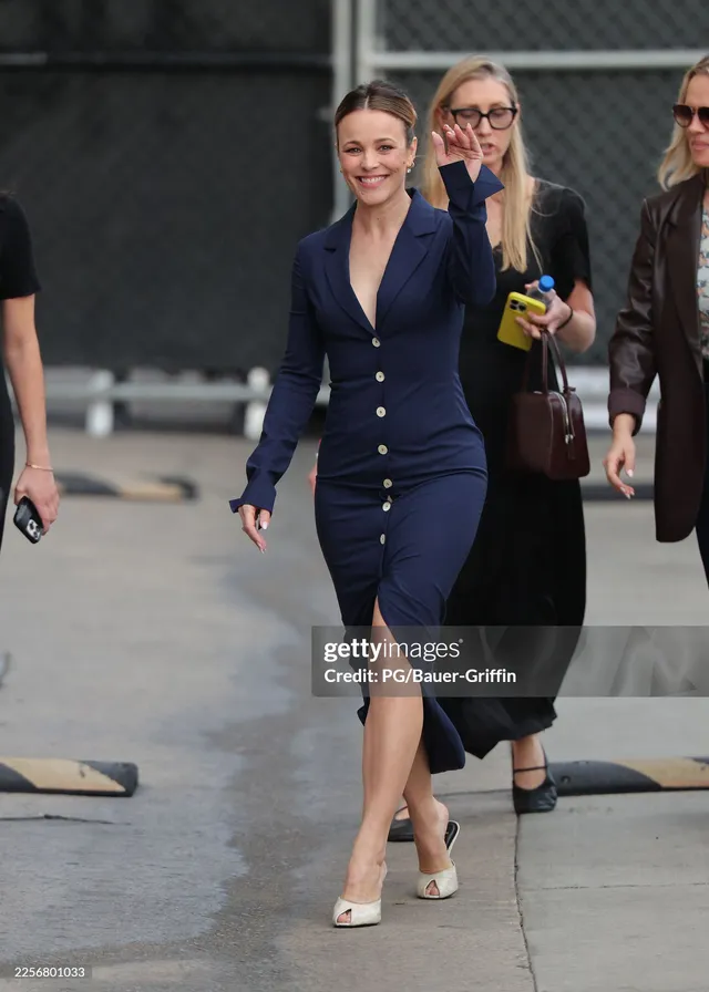 Rachel McAdams walking in a blue dress and white heels on a street.